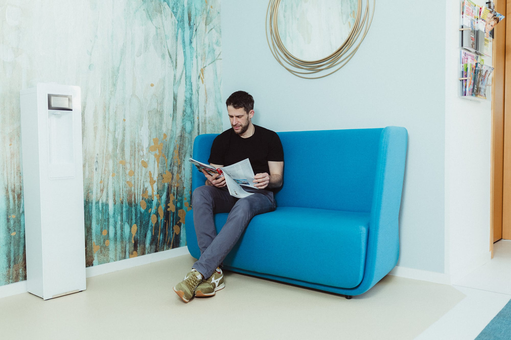 Hautarztpraxis Schönfeld & Hausmann. Ein Patient sitzt auf der blauen Couch im Wartezimmer